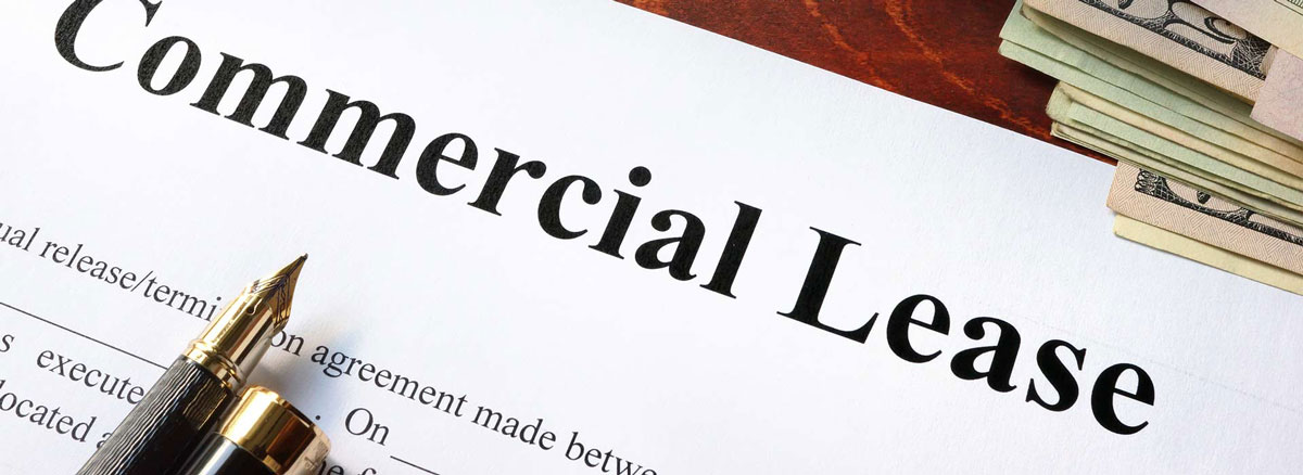 A commercial lease agreement sits on a wooden table next to a pair of glasses, money, and a pen.