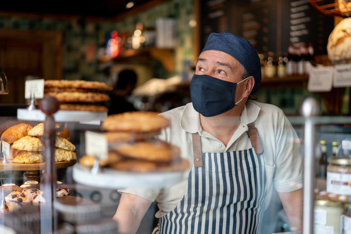 Restaurant owner wearing a face mask stands behind counter.