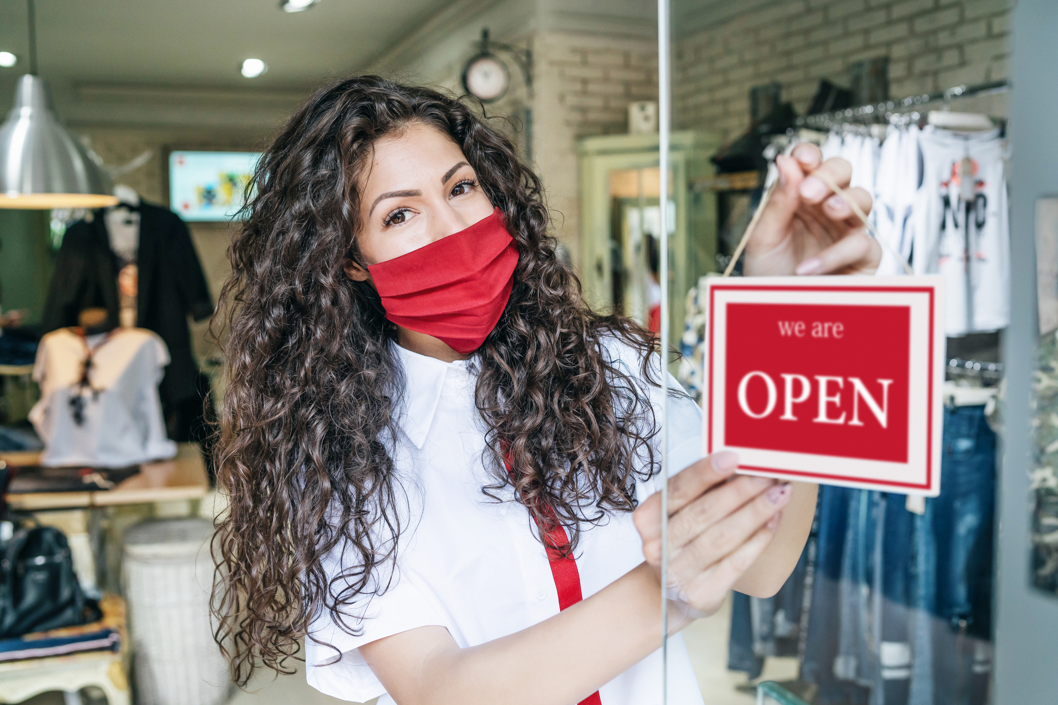 Woman wearing red face mask hangs an open sign on her business's front door.