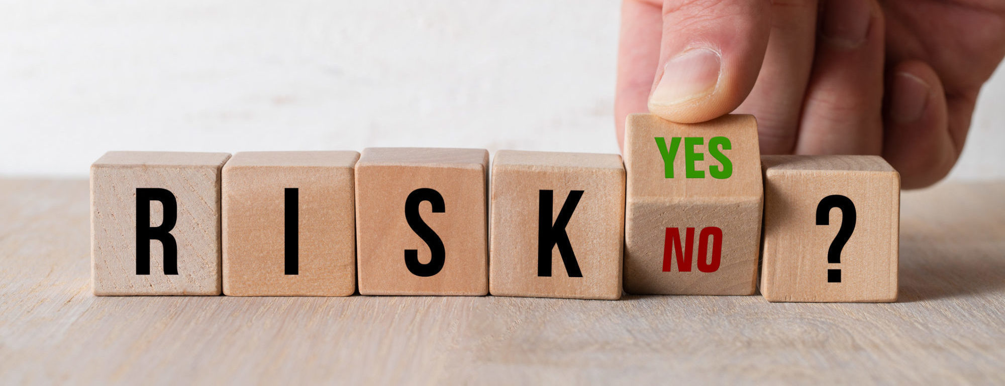 A hand turns a wooden cube with YES or NO written on it as an answer to the cubes before it that spell out RISK.