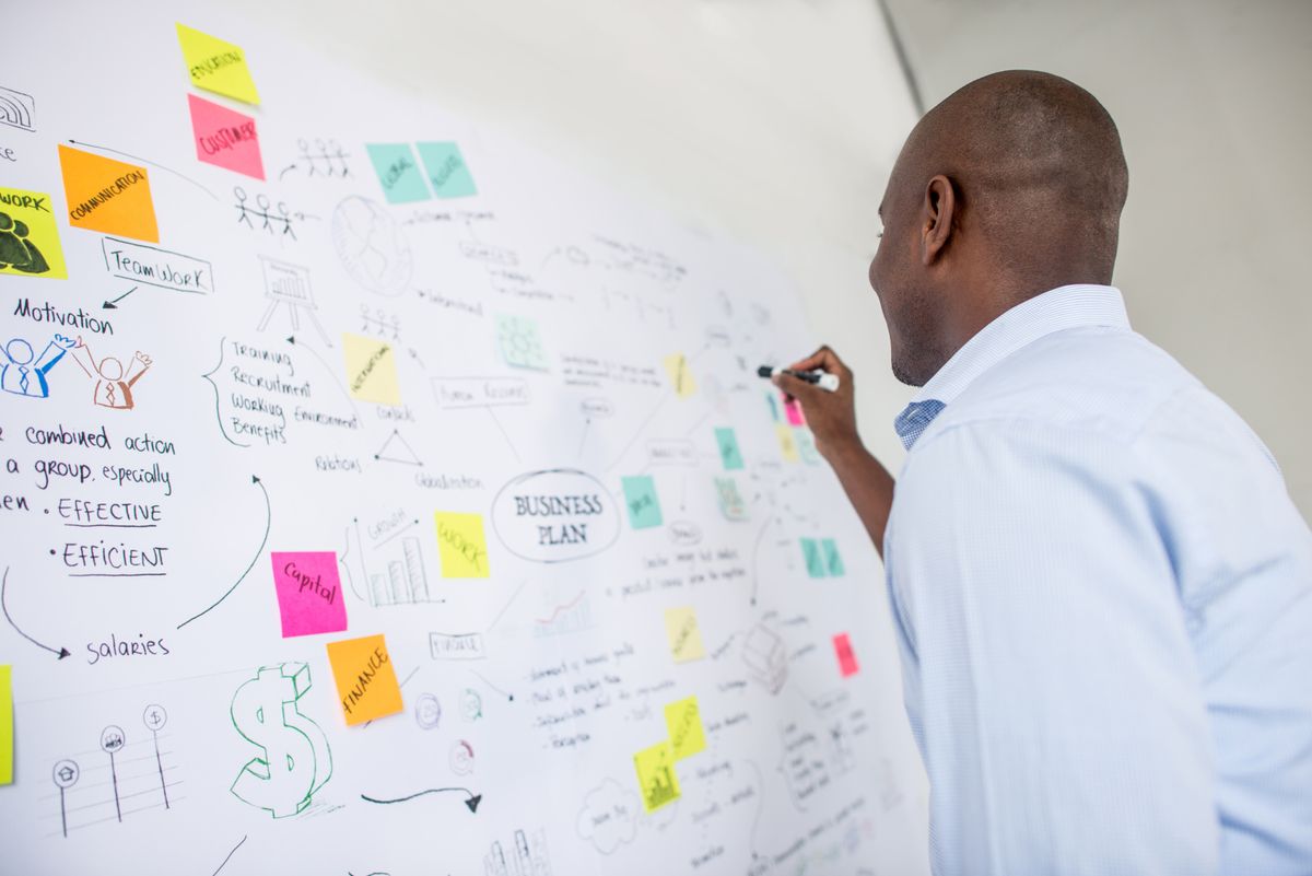 A man writes on a white board as he outlines a business plan.