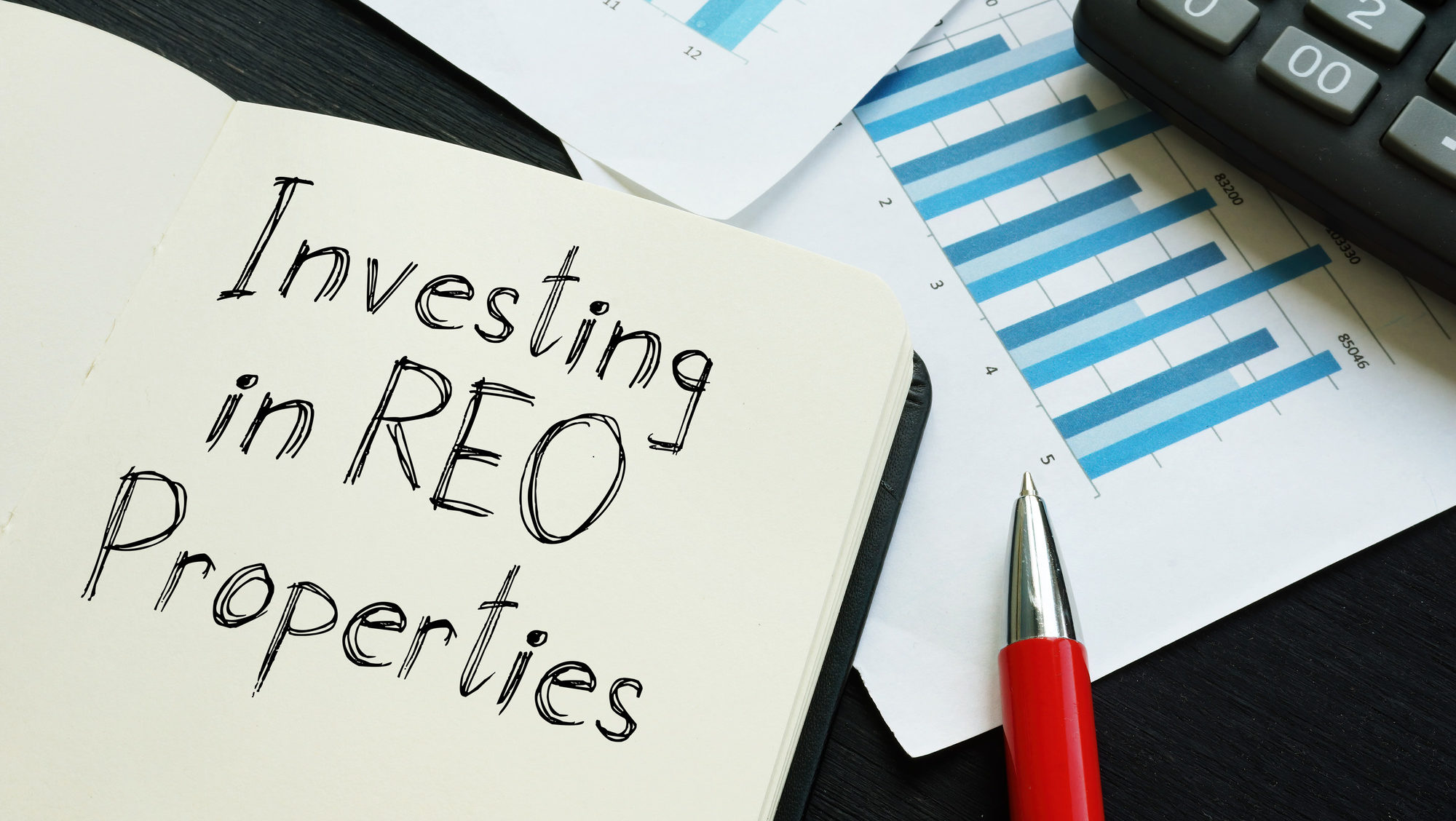 In an open lined notebook, "Investing in REO Properties" is written in black ink.